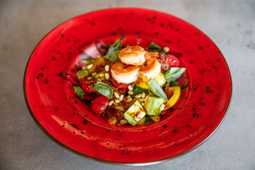 delicious and appetizing salad of shrimp, tomatoes, spinach, cheese, nuts, pate lies on a red plate...