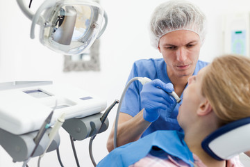 Male dentist treating young female patient in dental office