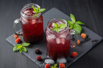 Fresh blackberry smoothie. Fresh summer cocktail with blackberry and ice cubes on a dark background on a black wooden table