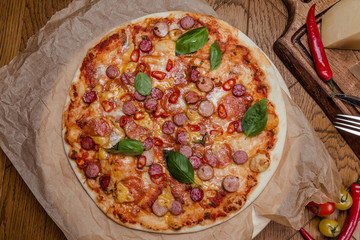 italian pizza with assorted sausages and hot pepper, the background is decorated with vegetables, on a wooden background