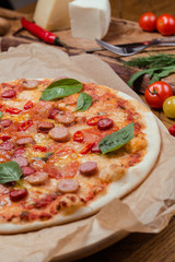 italian pizza with assorted sausages and hot pepper, the background is decorated with vegetables, on a wooden background