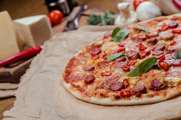 italian pizza with assorted sausages and hot pepper, the background is decorated with vegetables, on a wooden background