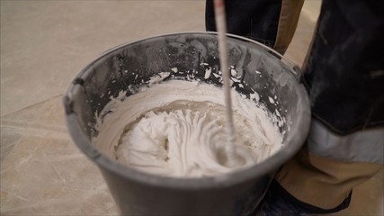 Mix the mixture in a black bucket. Worker mixes a solution in a black bucket. A man mixes a white mixture in a bucket. White substance in a black bucket.
