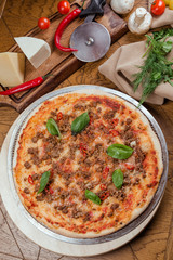 Pizza Bolognese with basil on a wooden board, background wooden decorated with vegetables and cutlery
