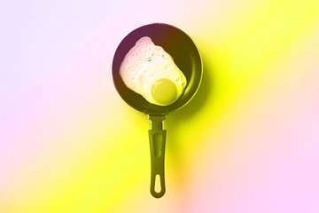 Creative food concept with fried egg on pan in trendy neon colors. Rainbow gradient background with...