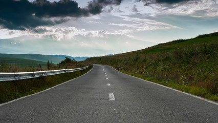 Empty rural asphalt road with green vegetation, clearing sky after summer rainstorm. 