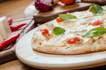 Pizza Margherita with basil on a wooden board, a wooden background decorated with vegetables and cutlery