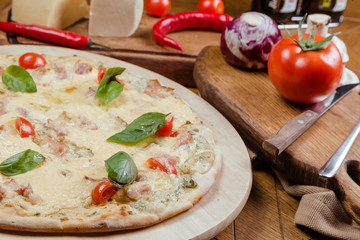 Pizza Margherita with basil on a wooden board, a wooden background decorated with vegetables and cutlery