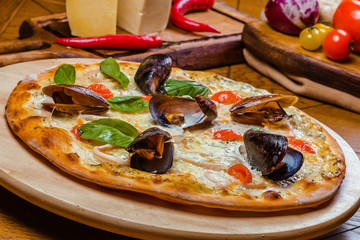 fresh delicious Italian Seafood pizza with mussels,cheese, colmar and basil on a wooden board,...