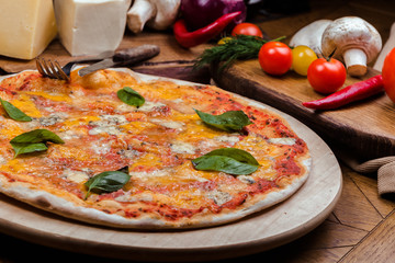 Pizza four cheeses with basil on a wooden board, wooden background decorated with vegetables and cutlery