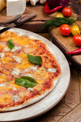 Pizza four cheeses with basil on a wooden board, wooden background decorated with vegetables and cutlery