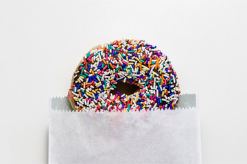 Chocolate donut with sprinkles in a white paper bag on a white background, creative minimal food...