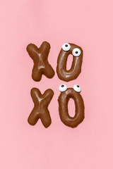 XOXO word made with chocolate biscuits on a pastel pink background, creative minimal Valentine concept