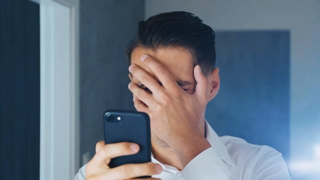 Shocked Man saw an unpleasant message on a smartphone. A man makes facespalm after a message is viewed on a smartphone. The concept of disappointment, shame and embarrassment.