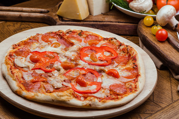 salami pizza on a wooden board, wooden background decorated with vegetables and cutlery