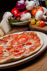 salami pizza on a wooden board, wooden background decorated with vegetables and cutlery
