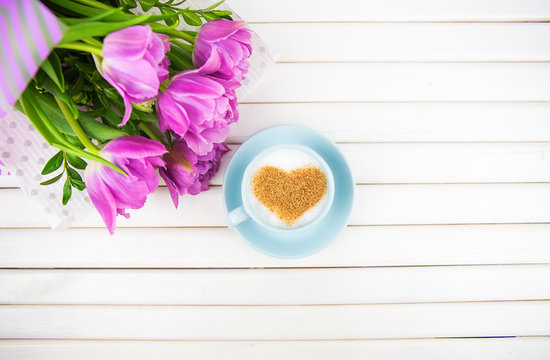 Cup of cappuccino with a heart shaped symbol and purple tulips on a wooden background