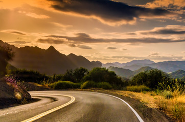California winding highway with overcast sky, mountains background, near sunset.