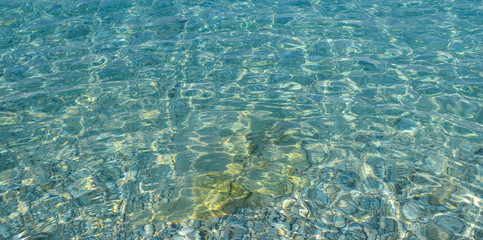Beautiful colorful pebbles and big stone under turquoise blue clear water, scenic marine background or texture, top view