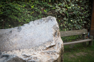Large stone to place an engraving, message, phrase. Green background and a wooden bench