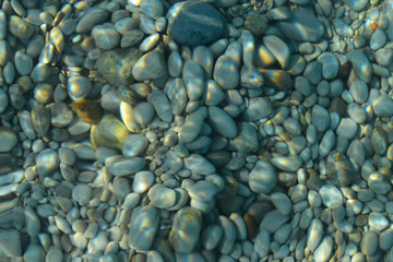 Beautiful colorful pebbles and big stone under turquoise blue clear water, scenic marine background or texture, top view