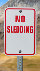 Vertical frame Close up of a No Sledding sign with a towering mountain in the background