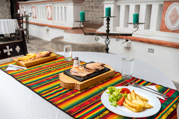 Table with colorful tablecloth containing a dish with chips with tomato and lettuce. The middle tray has pork and the bottom tray contains french fries with fish