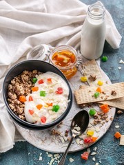Muesli or Granola with candied fruit in a dark bowl, homemade yogurt, orange jam and milk. Tasty and healthy breakfast concept. Vertical shot