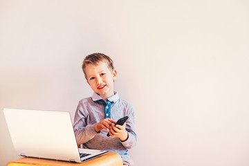 Happy funny child working as an executive with his laptop and his smart phone.