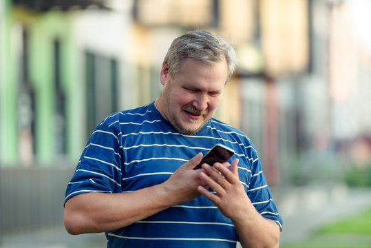 Man happily reads the SMS message on the smartphone on the street