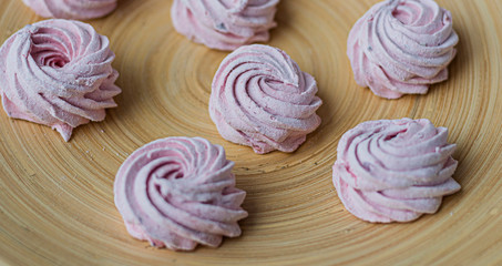 Obraz na płótnie Canvas Merengue Marshmallow Zephyr lined in a circle on a bamboo plate on a white wooden background. Flat lay. Top view. Pink sweet homemade zephyr or marshmallow.