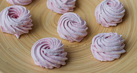 Merengue Marshmallow Zephyr lined in a circle on a bamboo plate on a white wooden background. Flat lay. Top view. Pink sweet homemade zephyr or marshmallow.