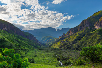 Green valley in the mountains with few white clouds overhead