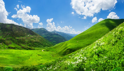 Beautiful green mountain valley. Scenic grassy mountains. Summer day in Georgia. Amazing bright mountain landscape. Green hills and clouds on blue sky - Powered by Adobe