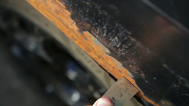 A man cleans rust on a car body with a scraper
