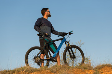 Cyclist in shorts and jersey on a modern carbon hardtail bike with an air suspension fork rides off-road on the orange-red hills at sunset evening in summer