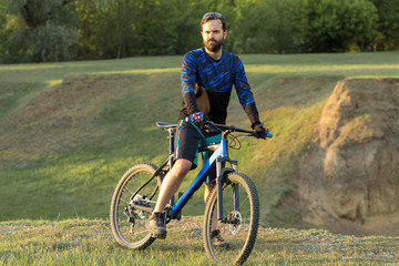 Fototapeta premium Cyclist in shorts and jersey on a modern carbon hardtail bike with an air suspension fork rides off-road on the orange-red hills at sunset evening in summer