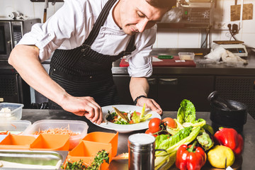 Professional chef cooking in the kitchen restaurant at the hotel, preparing dinner. A cook in an apron makes a salad of vegetables and pizza.