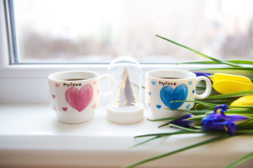 beautiful flowers-tulips and irises lie on the windowsill with two cups of coffee