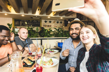 Group of young cheerful friends are sitting in a cafe, eating, drinking drinks. Friends take selfies and take pictures.