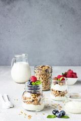 Jars with tasty parfait made of granola, berries and yogurt on stone grey table. Copy space.