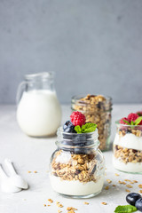 Jars with tasty parfait made of granola, berries and yogurt on stone grey table. Copy space.