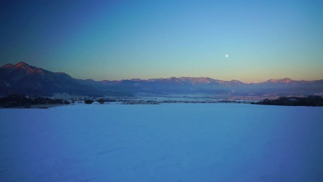 Snowy field and mountains at sunrise with full moon