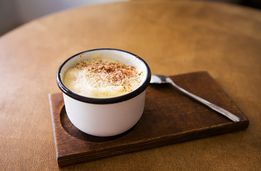 a cup of cappuccino stands on a wooden table and stands for a spoon