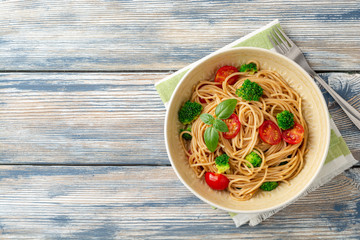 Whole wheat spaghetti pasta with broccoli, cherry tomatoes and basil in bowl on wooden background....