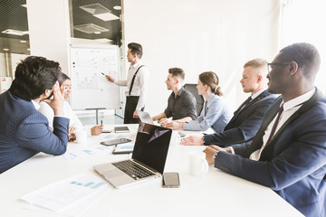 Company leader standing near the flipchart. A team of young businessmen working and communicating together in an office. Corporate businessteam and manager in a meeting.