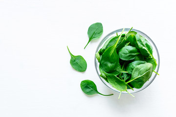 Fresh green spinach leaves in glass bowl on white table. Organic food, healthy diet, vegetarian food. Top view.