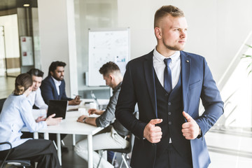 Business man stands on the background of partners. A team of young businessmen working and communicating together in an office. Corporate businessteam and manager in a meeting.