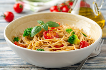 Whole wheat spaghetti pasta with broccoli, cherry tomatoes and basil in bowl on wooden background. Selective focus.