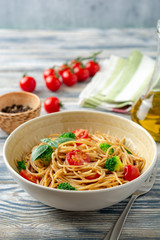 Whole wheat spaghetti pasta with broccoli, cherry tomatoes and basil in bowl on wooden background. Selective focus.